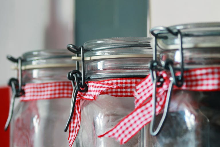 Three glass jars adorned with red gingham ribbons, ideal for kitchen storage or decoration concepts.